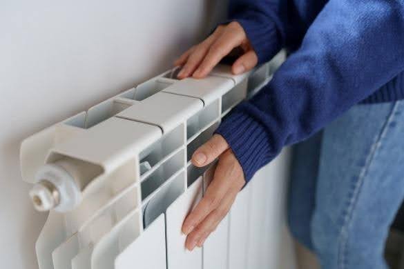 Someone touching a radiator in a blue jumper testing its temperature