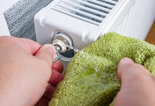 Closeup of someone bleeding a white radiator with a green cloth