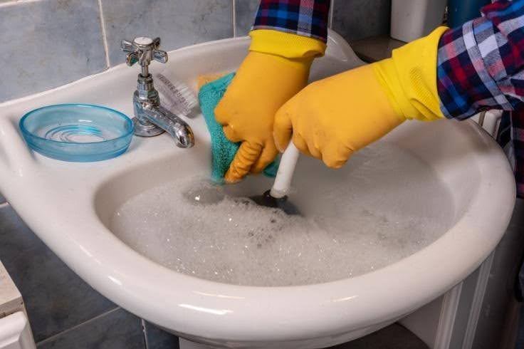 Closeup of someone wearing yellow globes and plunging an overflowing sink - How Do I Unblock a Sink Using a Plunger?